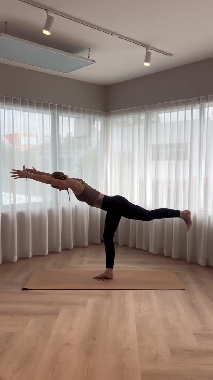 A woman holding a standing balance yoga pose in the studio