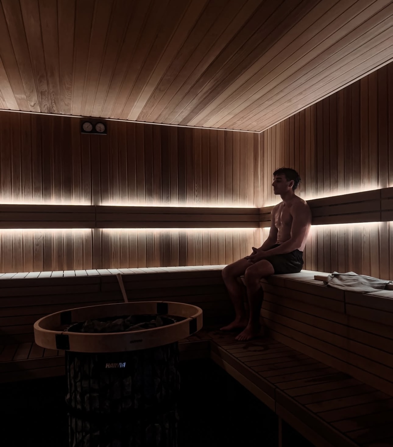 A person sitting on a bench in the sauna, with the sauna heater in the foreground